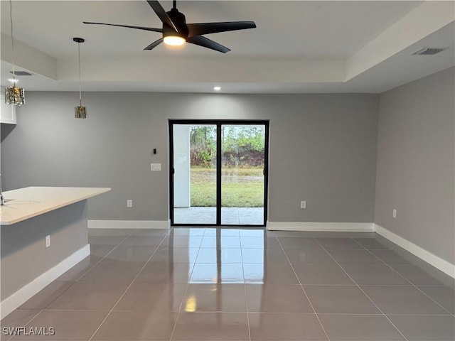 spare room with ceiling fan, a tray ceiling, and dark tile patterned floors