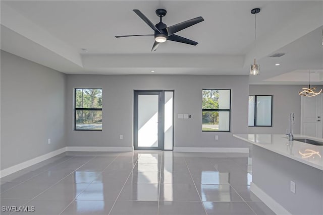 unfurnished living room featuring sink, a tray ceiling, ceiling fan, and light tile patterned flooring