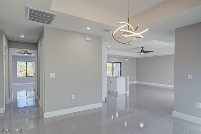 tiled empty room with a tray ceiling and ceiling fan with notable chandelier