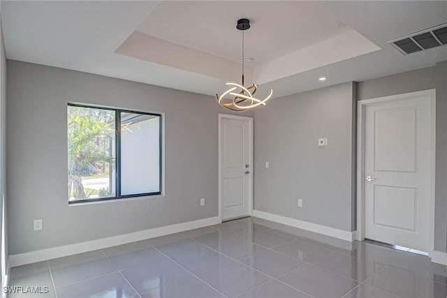 empty room featuring dark tile patterned floors, a tray ceiling, and a notable chandelier