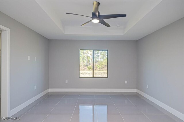 empty room featuring tile patterned flooring, ceiling fan, and a tray ceiling