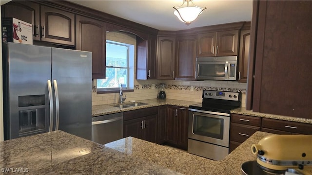 kitchen with dark brown cabinets, stainless steel appliances, light stone counters, and sink