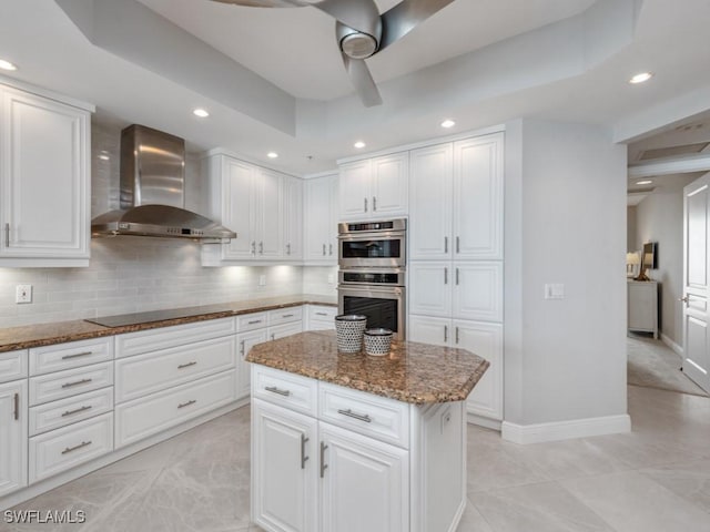 kitchen featuring black electric stovetop, wall chimney exhaust hood, double oven, white cabinetry, and a kitchen island