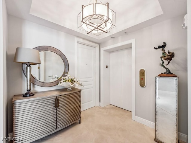 entrance foyer featuring a raised ceiling, elevator, and a chandelier