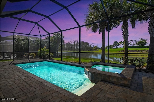 pool at dusk featuring a lanai, a patio area, an in ground hot tub, and a water view