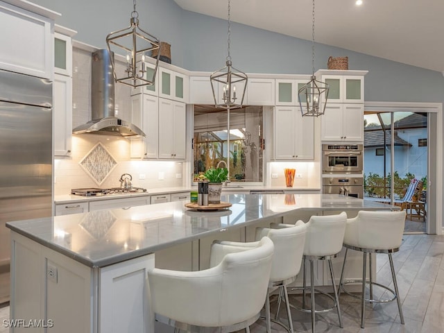 kitchen with appliances with stainless steel finishes, a spacious island, wall chimney range hood, white cabinets, and lofted ceiling