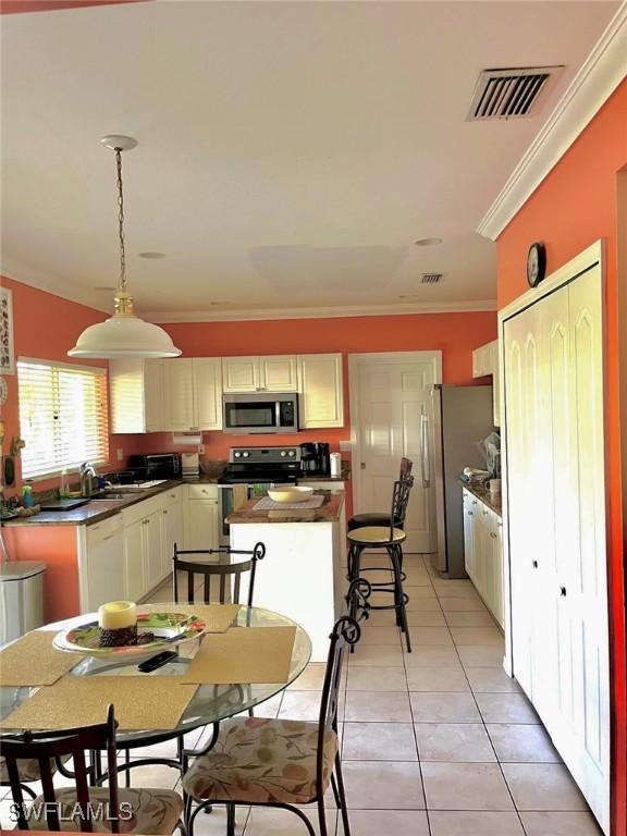 kitchen with light tile patterned flooring, pendant lighting, sink, stainless steel appliances, and crown molding