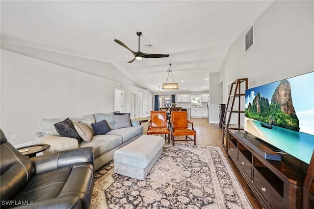 living area with baseboards, visible vents, light wood finished floors, ceiling fan, and vaulted ceiling