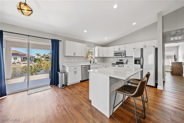 kitchen with a sink, wood-type flooring, appliances with stainless steel finishes, white cabinets, and light countertops