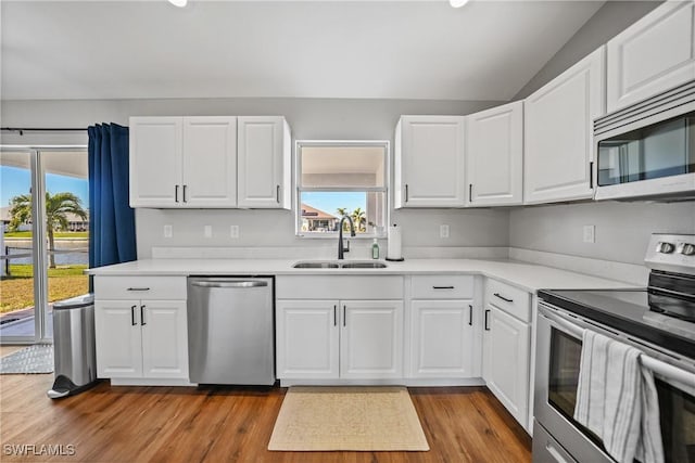 kitchen featuring lofted ceiling, appliances with stainless steel finishes, wood finished floors, white cabinetry, and a sink