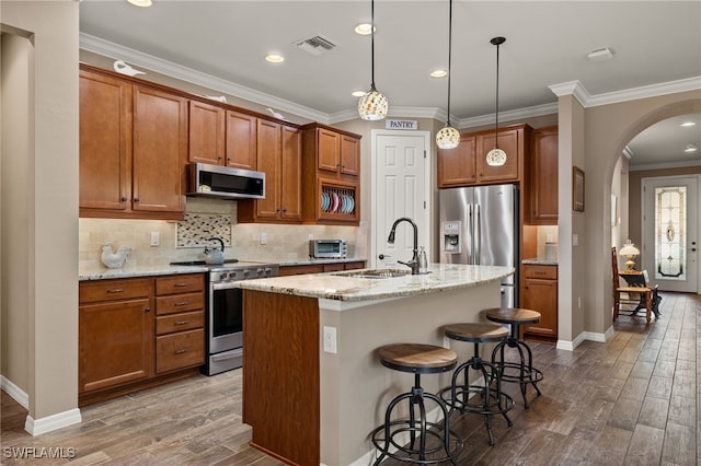 kitchen featuring light stone countertops, appliances with stainless steel finishes, a kitchen island with sink, sink, and hanging light fixtures