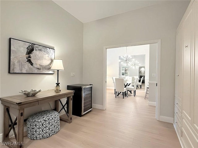 office space featuring light wood-type flooring, wine cooler, and an inviting chandelier