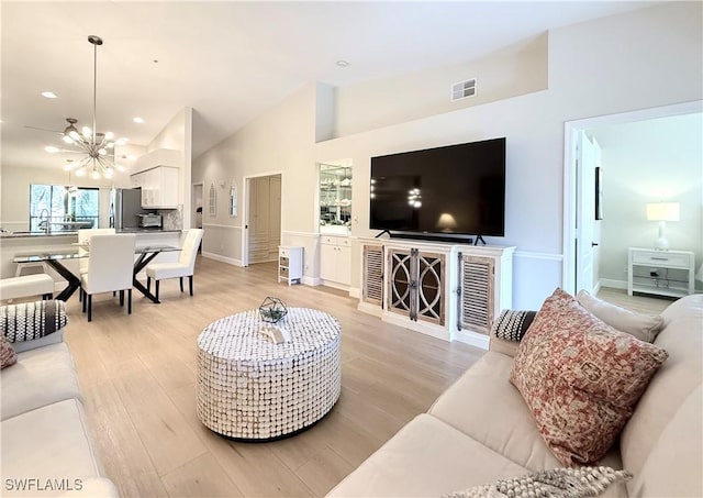 living room with a notable chandelier, lofted ceiling, and light wood-type flooring