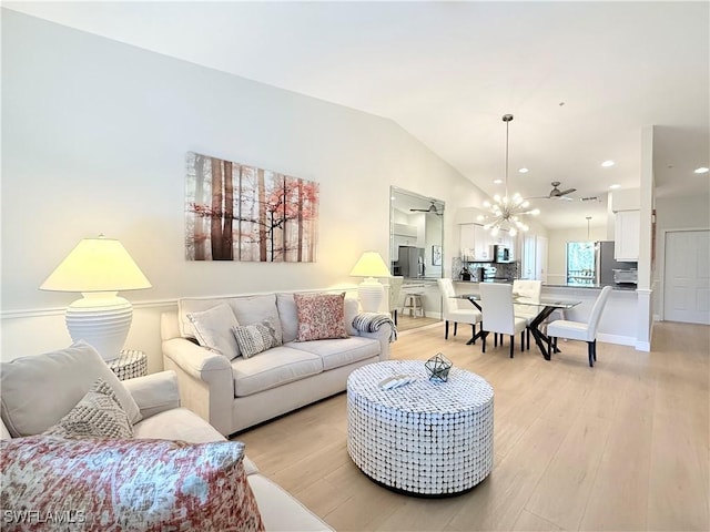 living room with ceiling fan with notable chandelier, light hardwood / wood-style floors, and vaulted ceiling