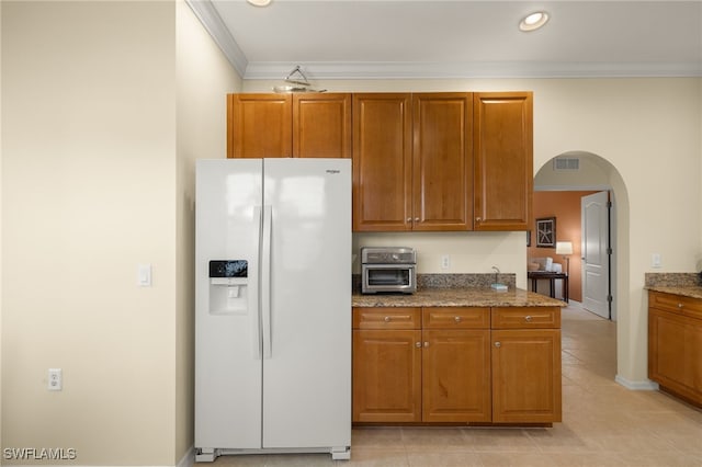 kitchen featuring stone countertops, white fridge with ice dispenser, light tile patterned floors, and ornamental molding