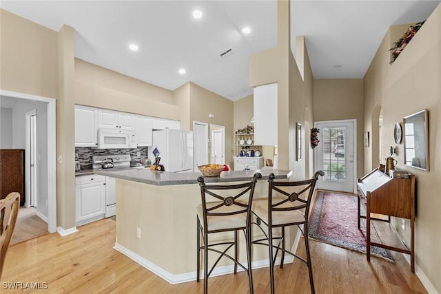 kitchen featuring white appliances, white cabinets, a kitchen breakfast bar, light hardwood / wood-style flooring, and tasteful backsplash