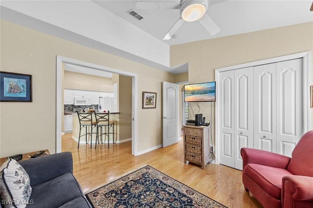 living room with ceiling fan, light hardwood / wood-style flooring, and vaulted ceiling