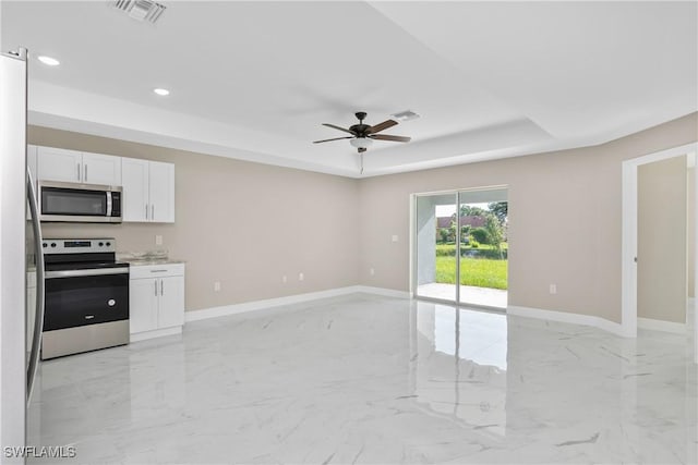 kitchen with white cabinets, ceiling fan, appliances with stainless steel finishes, and a tray ceiling