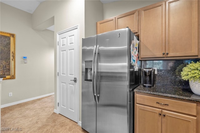 kitchen with decorative backsplash, stainless steel fridge, light tile patterned floors, and dark stone counters