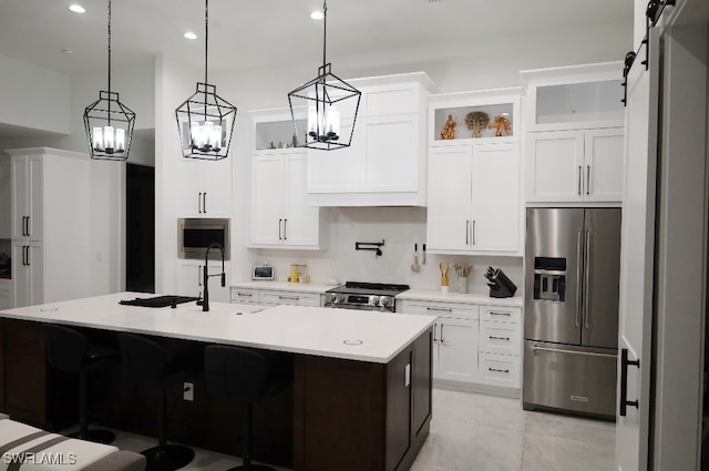 kitchen with white cabinetry, stainless steel appliances, a barn door, an island with sink, and pendant lighting