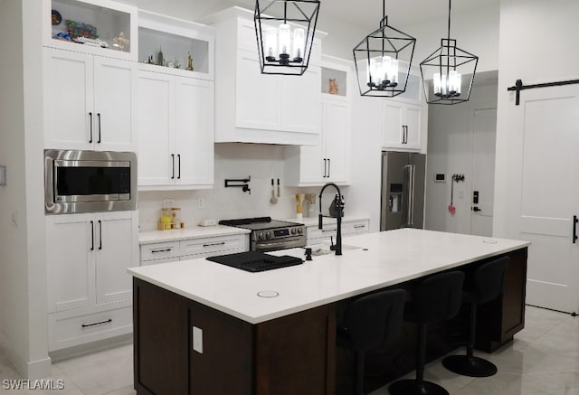 kitchen featuring white cabinetry, a barn door, a kitchen island with sink, and stainless steel appliances