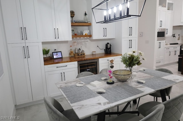 kitchen featuring stainless steel microwave, beverage cooler, hanging light fixtures, wooden counters, and white cabinets