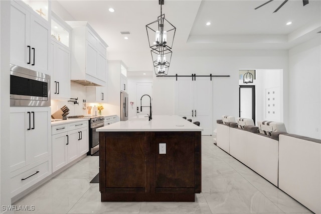 kitchen featuring an island with sink, light countertops, white cabinets, stainless steel appliances, and a sink