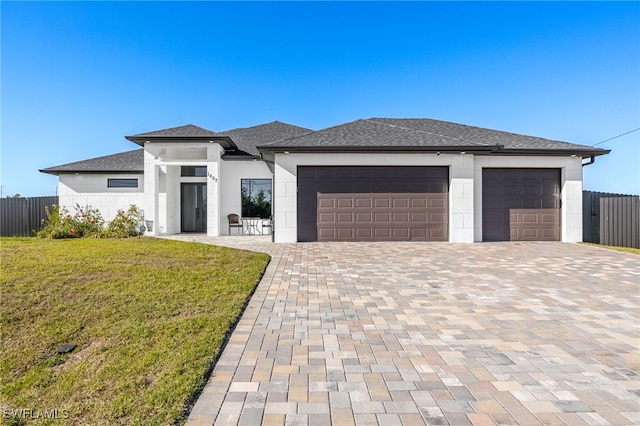 prairie-style house with fence, driveway, an attached garage, a shingled roof, and a front lawn