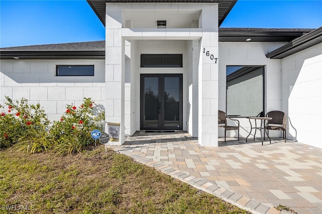 property entrance featuring french doors, a shingled roof, and concrete block siding