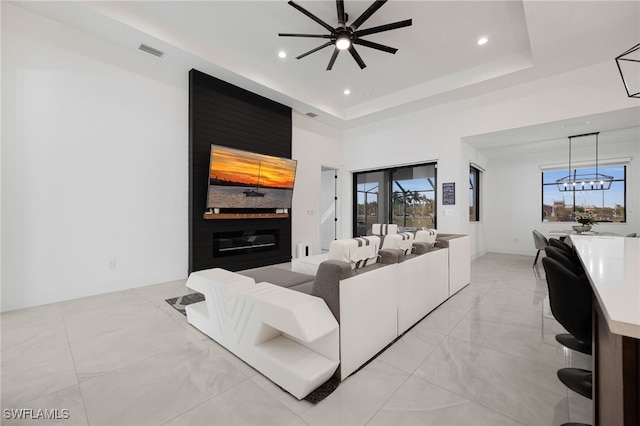 living room featuring a tray ceiling, recessed lighting, ceiling fan with notable chandelier, and visible vents