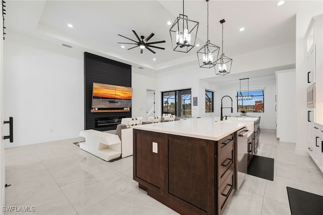 kitchen with an island with sink, open floor plan, light countertops, dark brown cabinets, and a chandelier