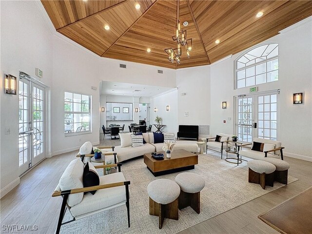 living room featuring french doors, a towering ceiling, wood ceiling, and a notable chandelier