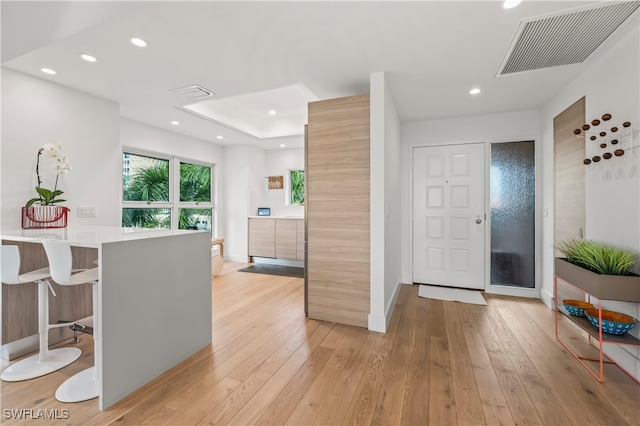 kitchen featuring a tray ceiling, a breakfast bar, kitchen peninsula, and light wood-type flooring