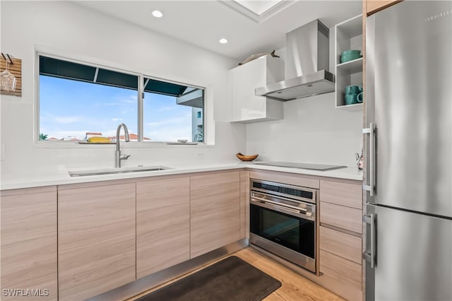 kitchen with light brown cabinetry, sink, light hardwood / wood-style flooring, appliances with stainless steel finishes, and wall chimney range hood