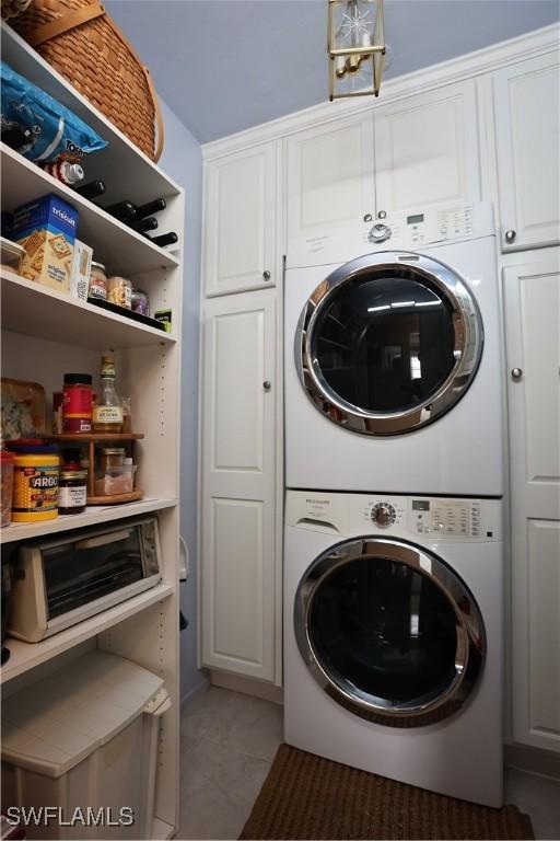 laundry room with cabinets, tile patterned flooring, and stacked washer / drying machine