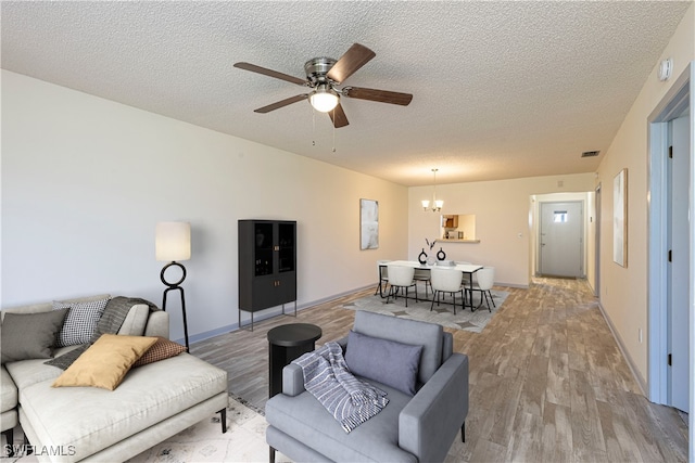 living room with ceiling fan with notable chandelier, a textured ceiling, and light hardwood / wood-style flooring