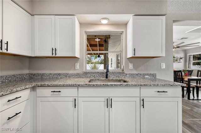 kitchen featuring sink, white cabinetry, light stone counters, light wood-type flooring, and ceiling fan