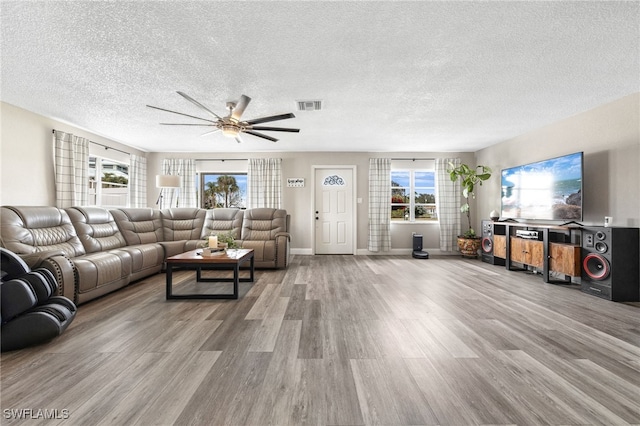 living room with ceiling fan, a textured ceiling, and light hardwood / wood-style floors