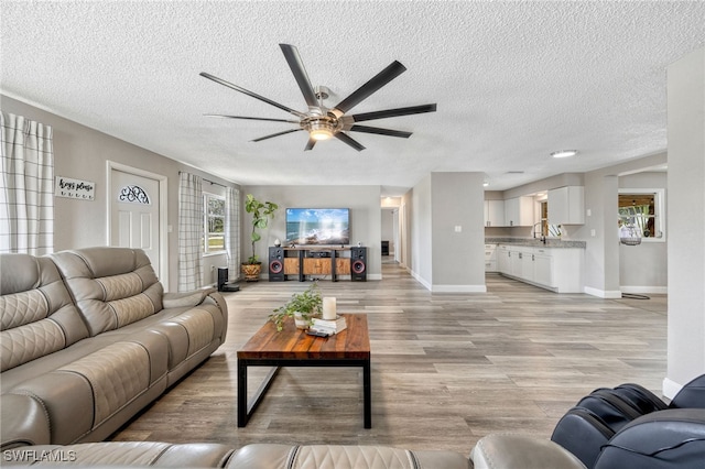 living room with ceiling fan, a textured ceiling, and light hardwood / wood-style flooring