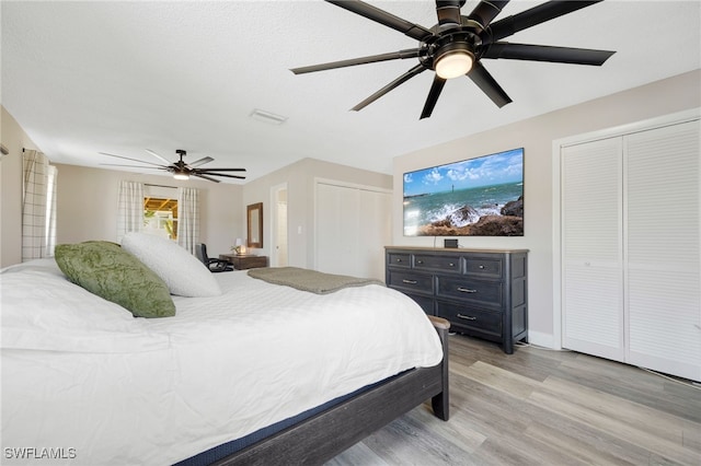 bedroom with multiple closets, light wood-type flooring, and ceiling fan