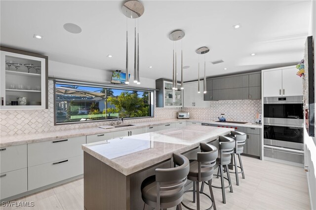 kitchen featuring decorative backsplash, light stone counters, decorative light fixtures, a kitchen island, and a kitchen bar