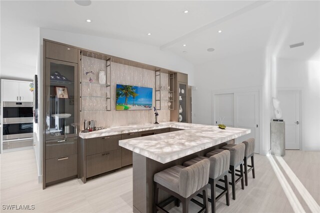 kitchen featuring decorative backsplash, a kitchen breakfast bar, double wall oven, lofted ceiling with beams, and a kitchen island