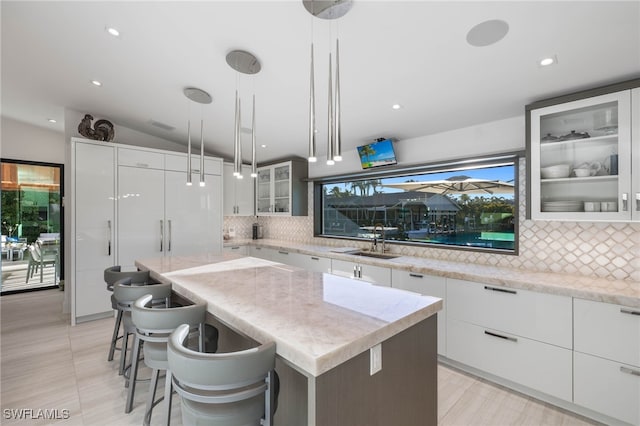 kitchen with pendant lighting, a kitchen island, light stone counters, white cabinetry, and a breakfast bar area