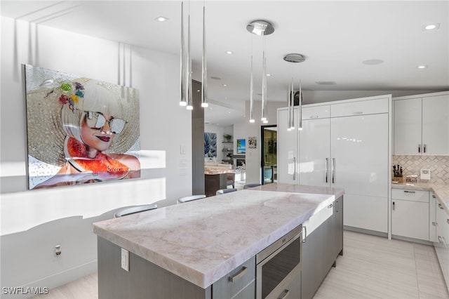 kitchen with a center island, hanging light fixtures, tasteful backsplash, lofted ceiling, and white cabinets