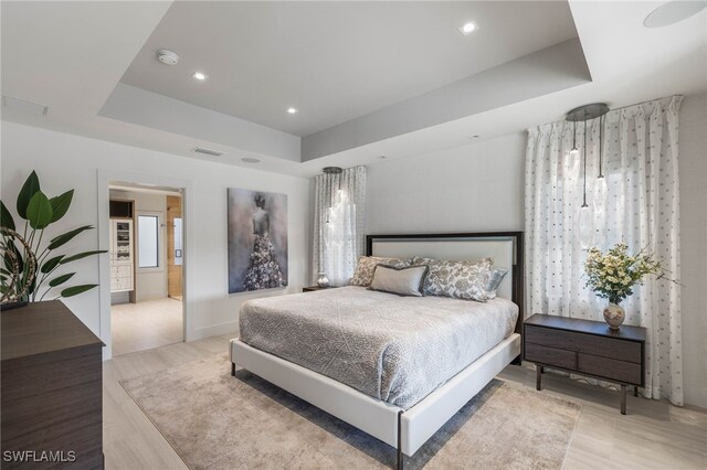 bedroom featuring a raised ceiling, connected bathroom, and multiple windows