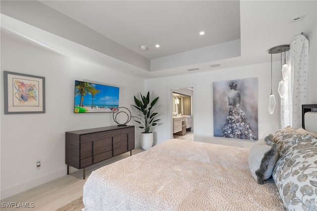 bedroom featuring light wood-type flooring, ensuite bathroom, and a tray ceiling