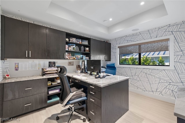 office space with a raised ceiling, light hardwood / wood-style flooring, and built in desk