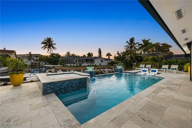 pool at dusk with an in ground hot tub, pool water feature, a water view, and a patio