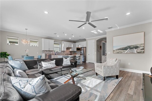 living room with light hardwood / wood-style flooring, ceiling fan with notable chandelier, and ornamental molding