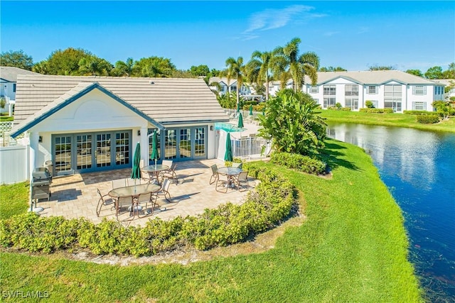 rear view of property featuring french doors, a yard, a water view, and a patio area